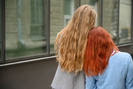 Same-sex relationships. A happy lesbian couple walked along the street and gently hugged each other around the waist. The backs of two beautiful women on a date. Two gay girls on a walkの写真素材