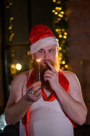 Santa with Christmas sparkles on holiday. A man with a red beard in a Santa Claus hat is celebrating the New Year. Happy New Year and Christmas.の写真素材