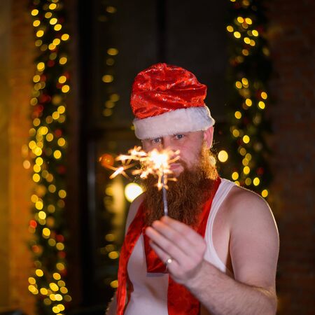 Santa with christmas sparkles. A man with a red beard in a Santa Claus hat jokingly makes a glamorous photo.の写真素材