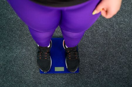 Fat woman is weighed in the gym. Top view on female legs in sneakers on electronic scales. Obesity.の写真素材