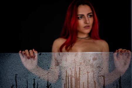 Beautiful naked woman holding a misted glass in her hands in drops of water. Focus on the glass. Black backgroundの写真素材