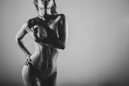 Beautiful naked female body with drops of milk on the skin. The girl in the shower. Water flows down a chic bust of a woman. Black and white.の写真素材