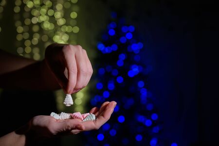 Close-up of female hands. A woman holds a handful of marshmallows in the shape of a Christmas tree on the background of Christmas lights.の写真素材