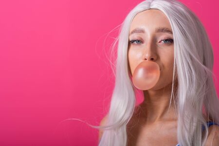 Portrait of a slender woman in a blonde wig posing on a pink background. Cute girl with blue eyes in...