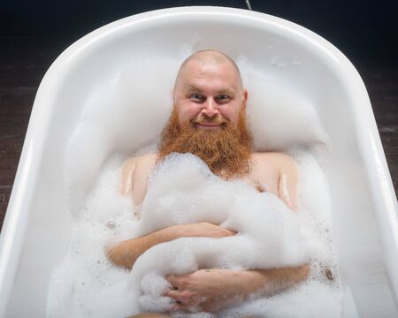 Portrait of a bald man fooling around in the foam bath. Top view on guy having fun in the bathroom.の写真素材