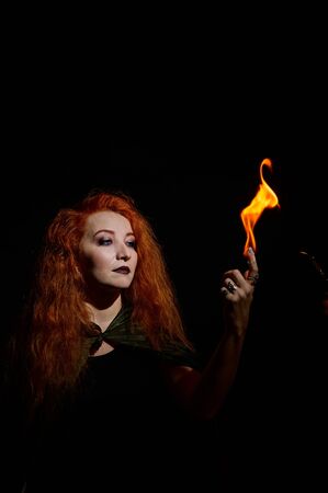 A witch with long curly hair holds a magic fire. Tongues of flame on the palms of a red-haired...
