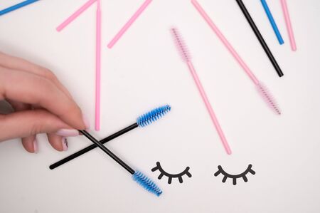 Top view of flatlay from eyelash extension tools. Female hand holds colored brushes for combing...