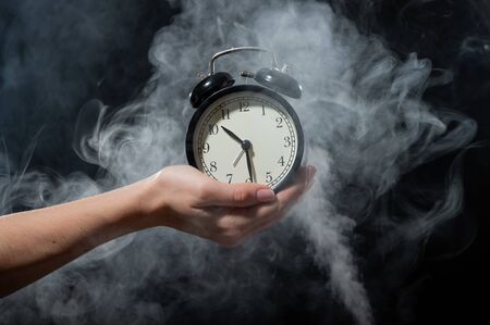 A woman holds an alarm clock in a studio full of smoke. White fog enveloped a round retro mechanical...
