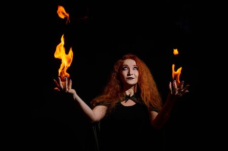 A witch with long curly hair holds a magic fire. Tongues of flame on the palms of a red-haired woman.の写真素材