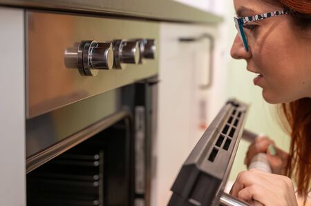 A young woman opens the oven. Housewife includes a built-in oven. Girl is cooking pastries.の写真素材