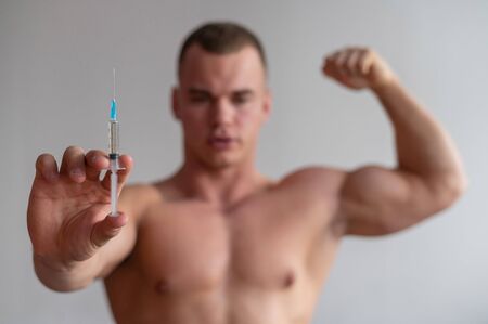 Attractive male bodybuilder with a naked torso holds a dope syringe. The athlete puts himself an injection of growth hormone.の写真素材