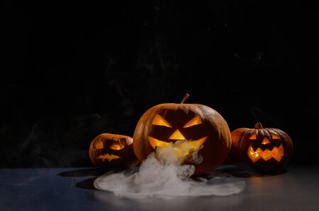 Halloween card. jack o lantern with candles glow on a black background. A row of creepy pumpkins with carved grimaces smokes in the dark.の写真素材