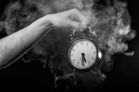 A woman holds an alarm clock in a studio full of smoke. White fog enveloped a round retro mechanical watch.の写真素材