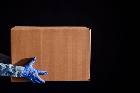 Closeup of female hands in gloves and a denim shirt. The delivery man passes the cardboard box to...