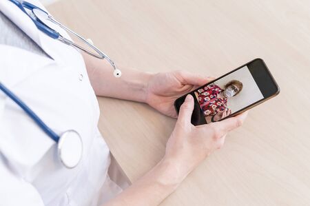 Unrecognizable female doctor conducts an online consultation on a smartphone. An elderly woman has a...