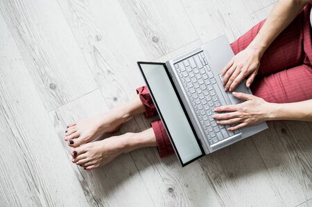 Top view of a faceless woman working from home. A girl sits on the floor in her apartment and works on a laptop. Work in quarantine.の写真素材
