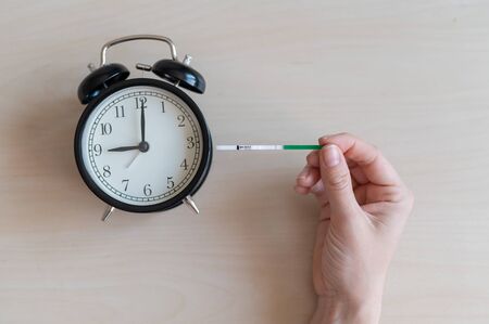 Woman holds a negative pregnancy test and alarm clock. Female fertility biological clock concept....