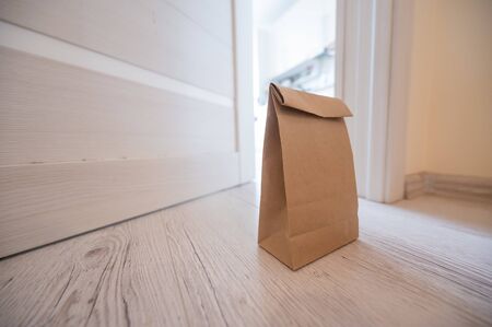 The concept of contactless delivery during the quarantine period. Kraft paper bag with online purchase at the open entrance door in case of danger of the spread of coronavirus.の写真素材