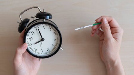 Woman holds a positive pregnancy test and alarm clock. Nine months of pregnancy. The concept of the biological clock of fertilityの写真素材