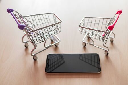 Top view on a shopping cart and mobile phone on a wooden table. Smartphone online shopping. Online shopping.の写真素材