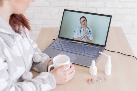 A woman with a cold is on sick leave and is looking at a laptop video consultation doctor. A patient at a remote appointment. Online meeting.の写真素材