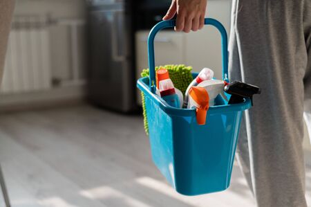 House cleaning concept. Faceless woman holds cleaning products in a blue basket. Closeup of the hands of a female workers house.の写真素材