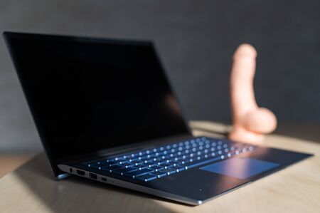 Blurred cyber leather dildo on the table behind a laptop. The concept of online sex. Artificial penis for female self-satisfaction.の写真素材