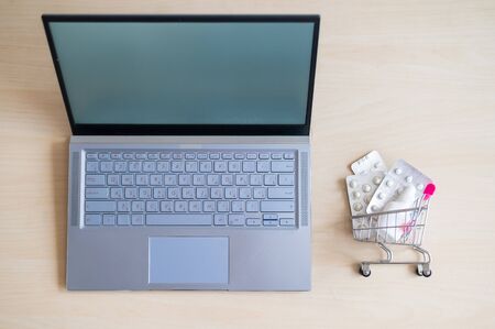 Online pharmacy concept. Top view of a laptop and a shopping cart full of medicines on the desktop. Buying pills on the Internet with home delivery.の写真素材