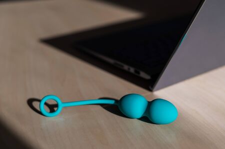Blue silicone vaginal kegel balls on a table next to a laptop. Sex toy for building is synchronized with a computer. Intimate muscle trainer for women health.の写真素材