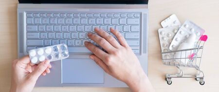 Online pharmacy. Closeup of female hands with a blister of tablets on a laptop keyboard. A woman chooses medicines on the Internet with home delivery.の写真素材