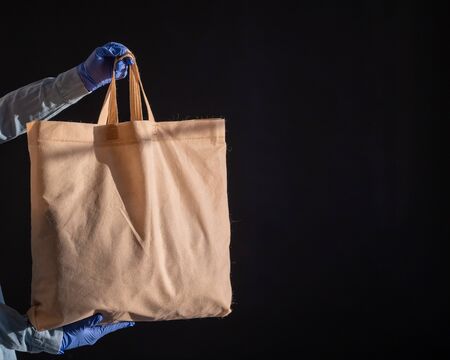 A bag of cotton fabric on a black background. The courier holds a canvas cloth bag without plastic...