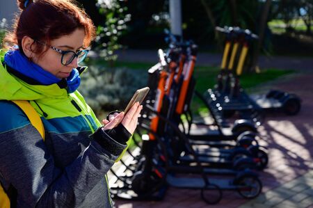 The girl in the jacket uses the mobile application to pay and unlock the rental electric scooter....