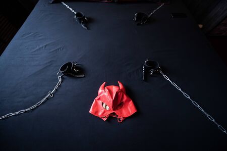 BDSM equipment. Top view of a red leather devil mask and black handcuffs with chains on a gray sheet. Sex toys. Dominance. No people.の写真素材