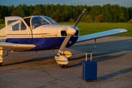 A blue suitcase and a landed small private jet. Four-seater plane with a propeller for the air taxi. Self travel concept. Airplane for VIP persons.の写真素材
