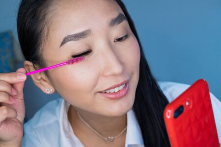 Beautiful Asian woman combing her eyelash extensions with a pink brush. Portrait of a girl taking a...