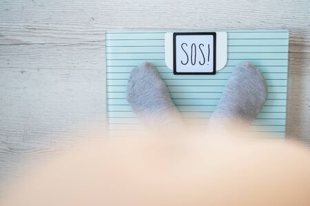 A woman in gray socks is standing on an electronic scale. Top view on the legs and bare belly of an obese woman. The word sos on the scales display.の写真素材