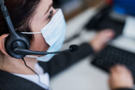 Close-up of a woman in a medical mask talking on a headset in an office. Portrait of a female call...