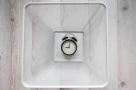 Top view of an alarm clock discarded in a white mesh metal trash bin. The concept of wasted time.の写真素材