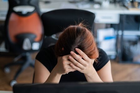 Tired woman workaholic t-shirt in an empty office. Female IT manager in casual clothes at computer. A girl with a headache works overtime. Migraine and depression due to problems at workの写真素材
