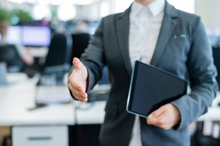 Woman office worker holds out her hand for greeting. Faceless business lady is holding a digital tablet and a handshake in an agreement to a successful transaction.の写真素材