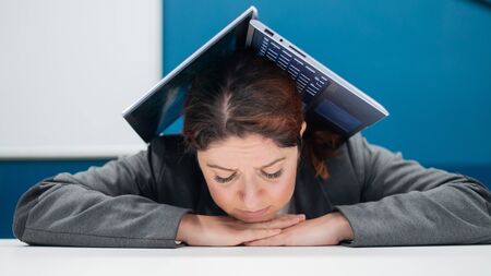 Problems at work. An exhausted woman folded her laptop over her head at her desk. Businesswoman in...