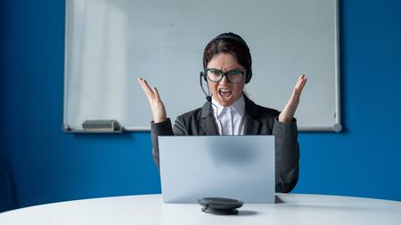 An angry woman in a headset is having an online conversation on a laptop in a conference room....