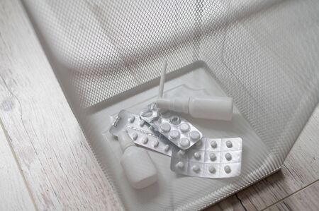 Medication in a white mesh metal wastebasket. Pills thrown into the trash. A paper basket with medicines inside on a wooden floor.の写真素材