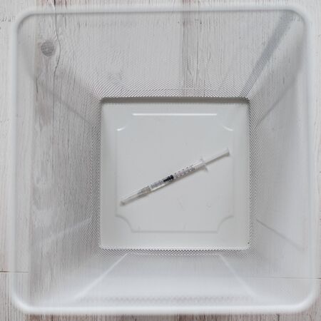The used insulin syringe is thrown into a white mesh metal waste bin. Top view of a trash bin on a wooden floor. Injections for diabetics.の写真素材
