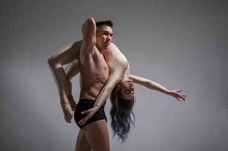 Heavy circus pose. A young man holds a flexible woman. Two acrobats or ballet dancers posing on a white background. A pair of gymnasts perform art.の写真素材