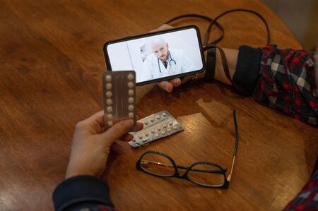 Online medicine. An old woman with coronavirus symptoms is talking on a smartphone with a virologist. Male doctor listens to complaints about the health of an elderly woman on the video link.の写真素材