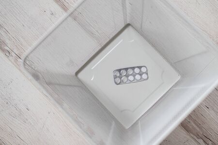 Medication in a white mesh metal wastebasket. A blister of pills thrown into the trash. A paper...