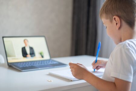 The boy communicates with a female teacher on a laptop webcam. Online lesson. Distance education in...