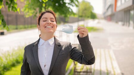 Contented woman walks outdoors while maintaining a social distance. A smiling female office worker is enjoying the freedom of taking off the mask. Coronavirus is defeated. The end of the working day.の写真素材