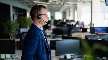 Portrait of a male call center operator in headset at workplace. A man works in an open space office...